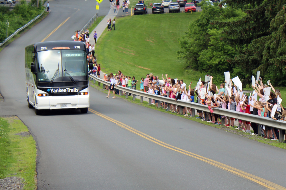 bus rolling pass line of cheering students and staff holding signs