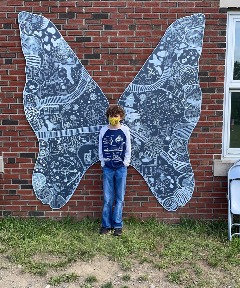 boy standing in front of giant wings attached to wall behind him