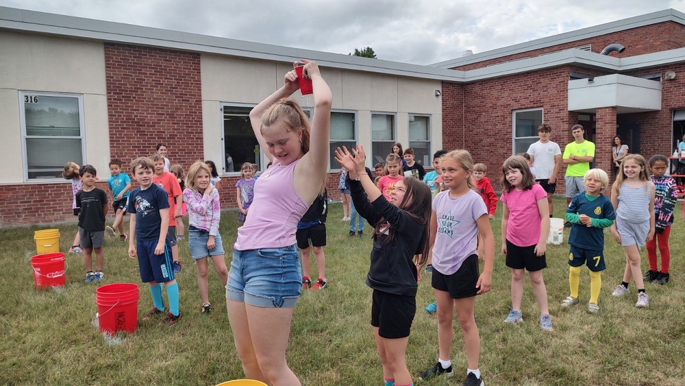 Middle school age girl playing field day games with elementary school, students 