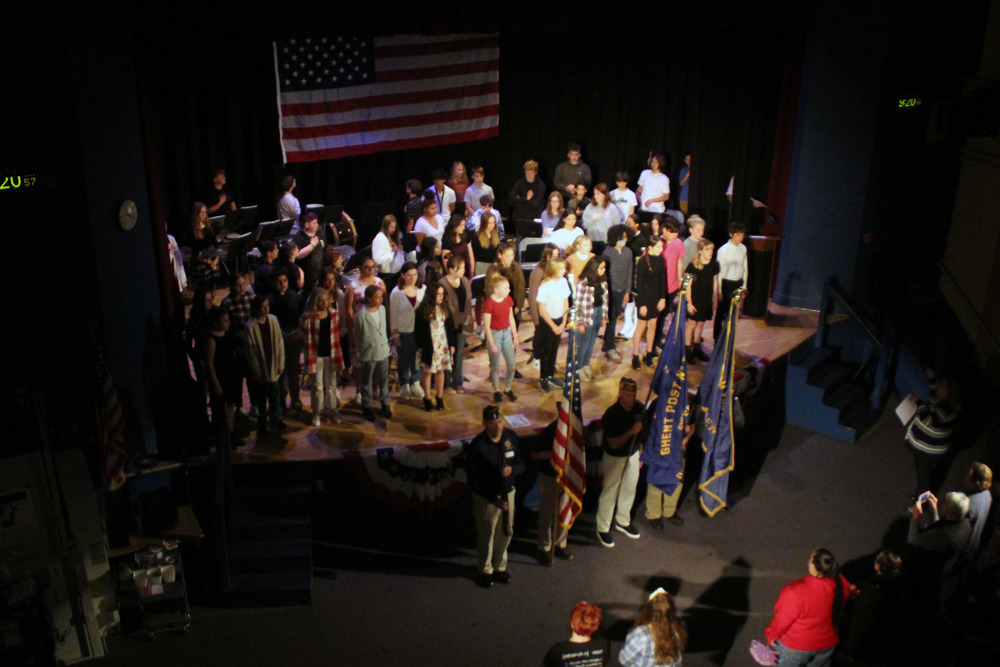 students sing on stage behind VFW color guard
