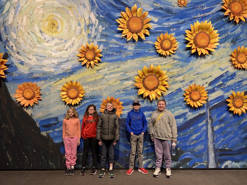 Student pose for photo in front of Van Gogh sunflowers exhibit