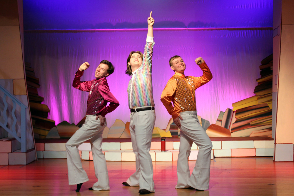 Three teenage boys in disco cloths singing on stage