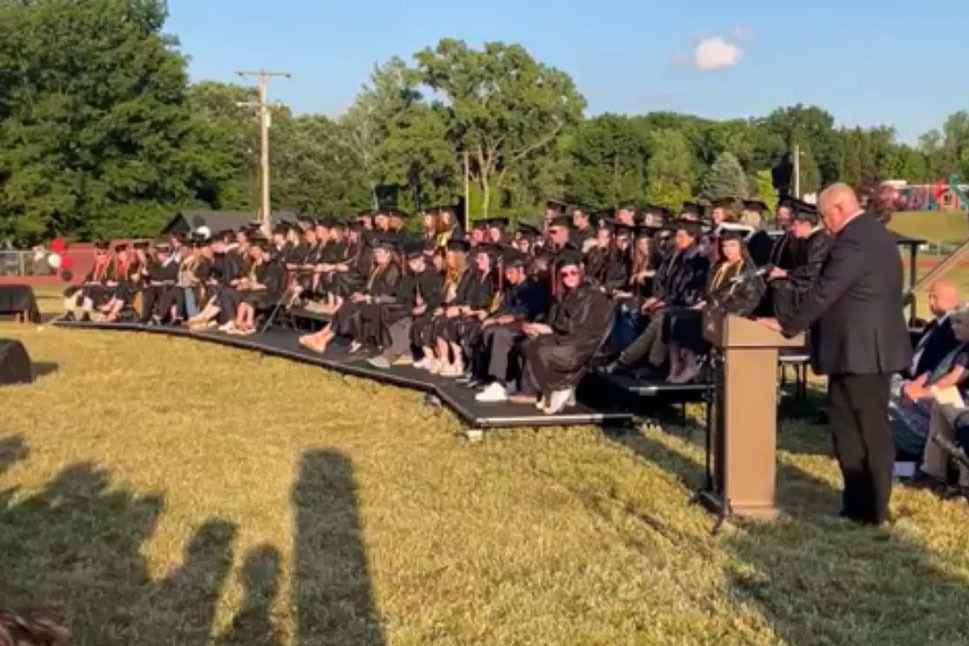 graduates in caps and gowns seated on bleachers