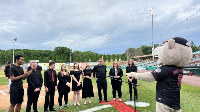 Students sing national anthem at baseball stadium with cat mascot
