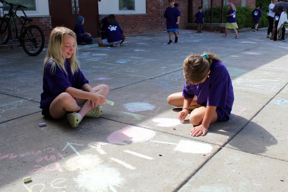 two girls writing in chalk on sidewalk