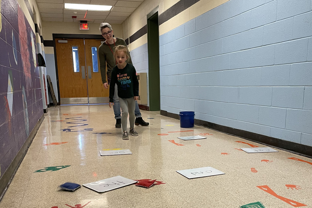 woman and girl throwing bean bags at word cards on floor