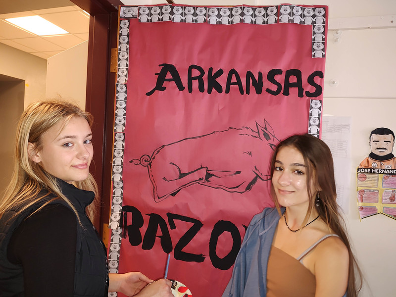 two girls pose with door decorated for Arkansas State