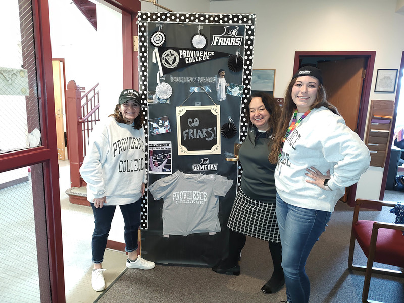 Three faculty members pose for photo wearing College sports shirts