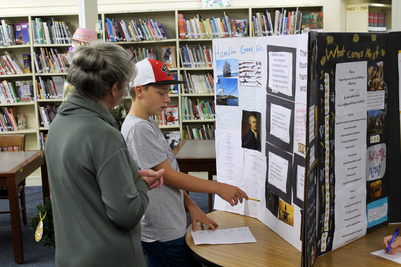boy explaining poster board display to woman