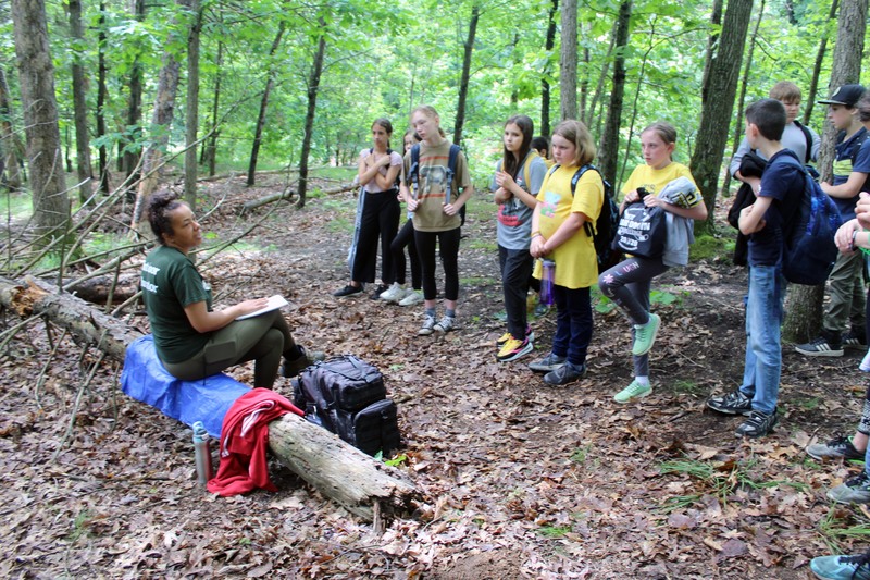 woman talks with students in woods