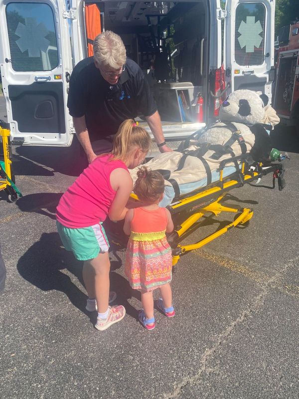 man showing girls stretcher behind ambulance