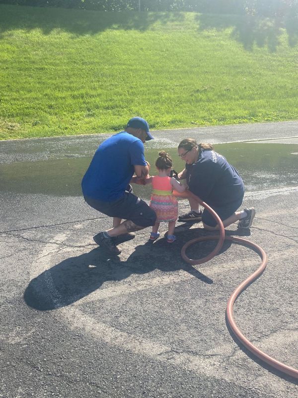 man and woman helping toddler handle fire hose