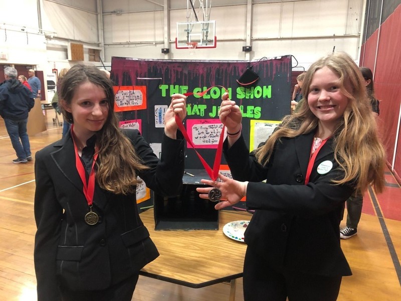 Two girls holding medals in front of Glow Show science project