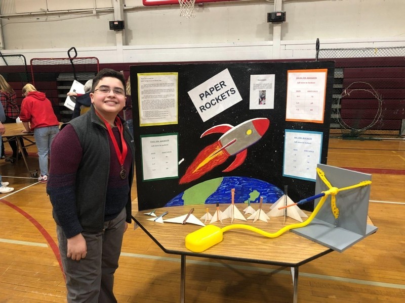 boy wearing medal next to paper rockets technology project
