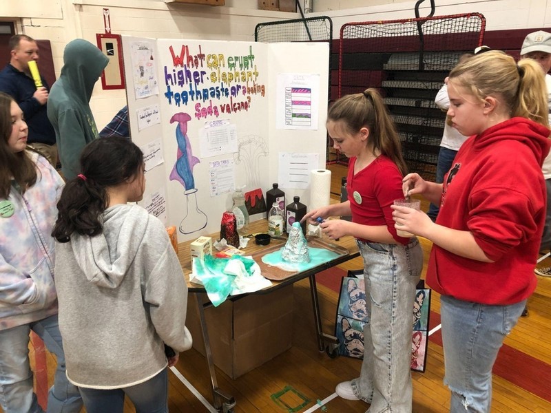 girl demonstrates volcano project to group of other girls