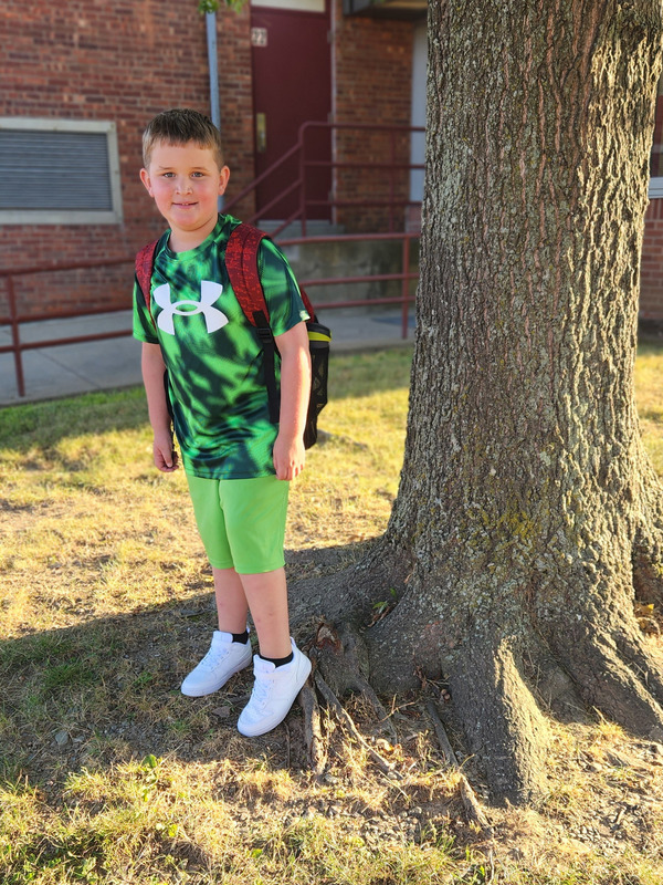 boy standing by tree in front of school
