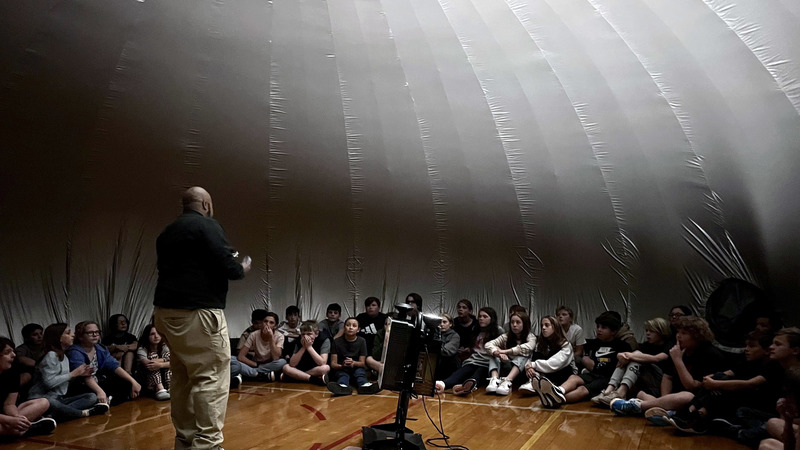 man giving presentation to a group of students inside a large inflatable planetarium