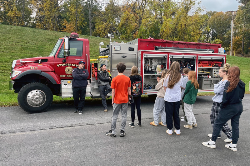 Fire department members talk with art class in front of fire truck