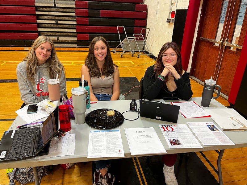 three girls sitting at registration table in gym